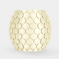 A round, textured ceramic planter or candle holder in a pale cream color, featuring a raised scale-like pattern, set against a solid light gray background.